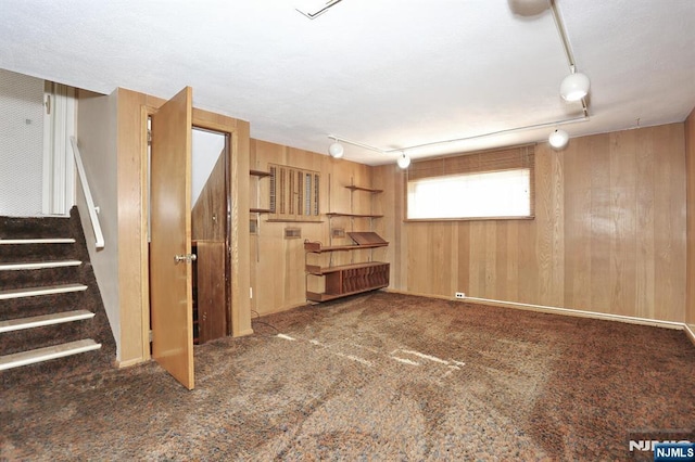 basement with rail lighting, dark carpet, and wood walls