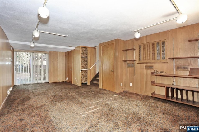 unfurnished living room with dark colored carpet, track lighting, and wood walls