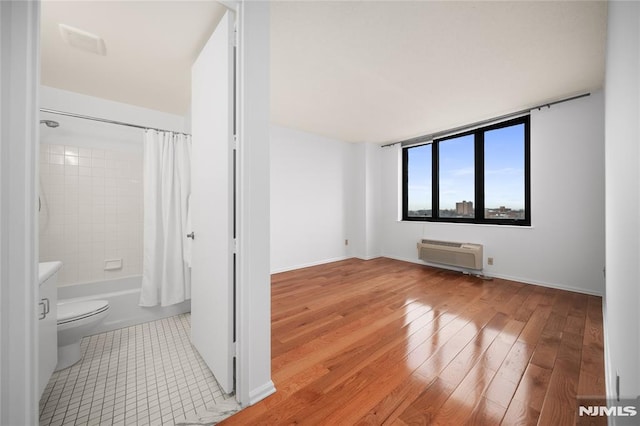 bathroom with a wall mounted air conditioner, wood-type flooring, shower / tub combo, and toilet