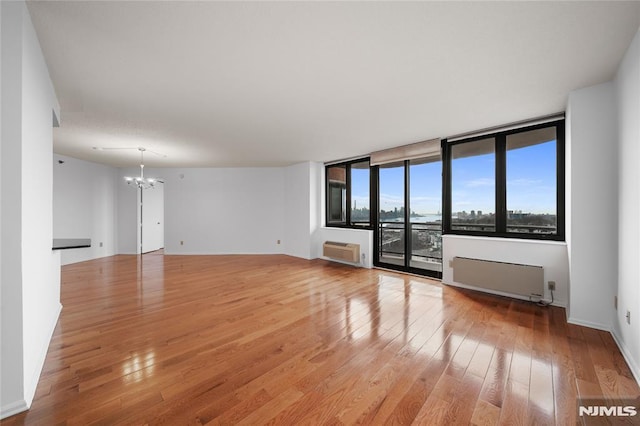 unfurnished room with a chandelier, light wood-type flooring, a wall mounted AC, and radiator