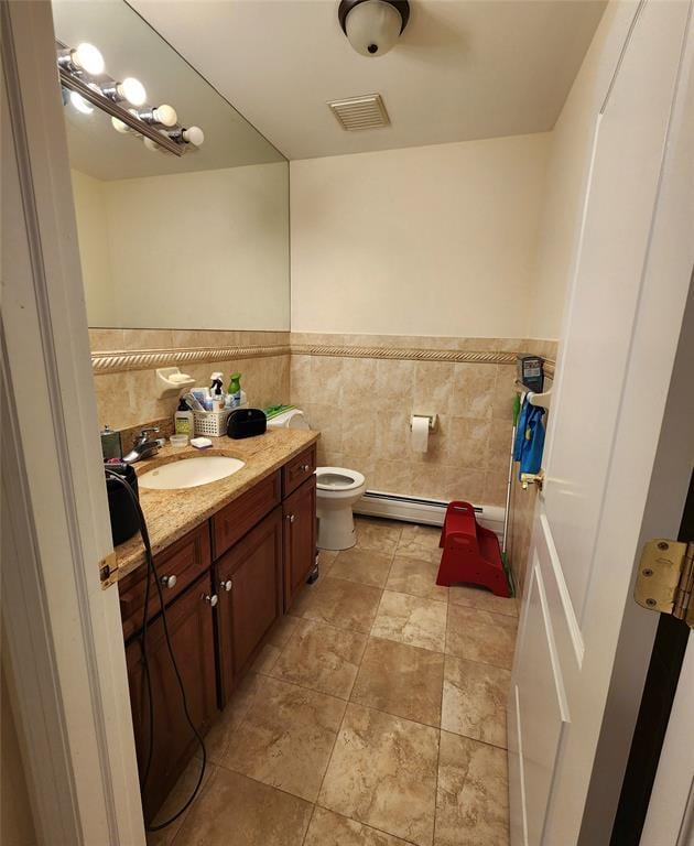 bathroom featuring vanity, tile walls, baseboard heating, and toilet