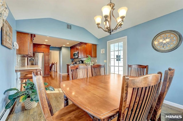 dining room featuring light hardwood / wood-style floors, an inviting chandelier, and vaulted ceiling