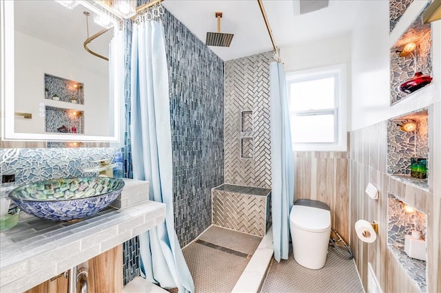 bathroom with a tile shower, toilet, and tile walls