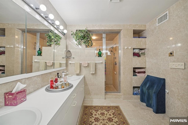 bathroom featuring tile patterned flooring, vanity, a shower with shower door, and tile walls