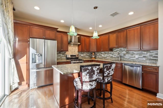 kitchen featuring stainless steel appliances, a center island, a breakfast bar, light stone counters, and wall chimney range hood