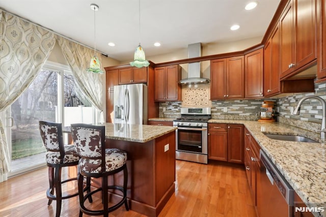 kitchen featuring light stone countertops, hanging light fixtures, wall chimney range hood, appliances with stainless steel finishes, and sink