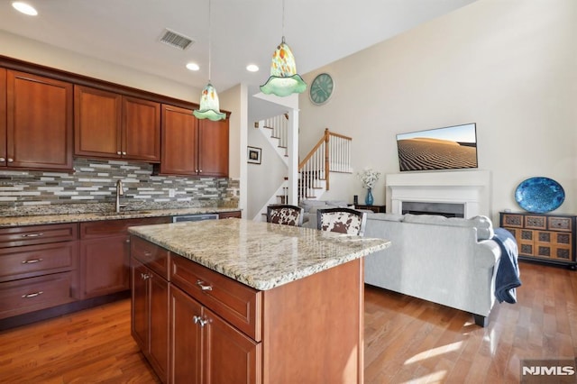 kitchen featuring pendant lighting, light stone counters, decorative backsplash, a kitchen island, and sink