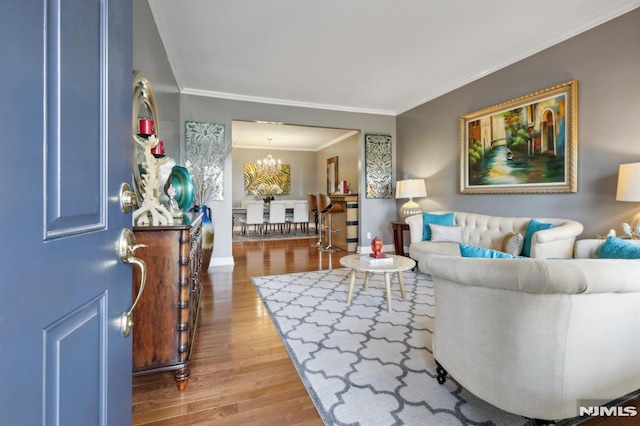 living room with wood-type flooring, an inviting chandelier, and ornamental molding