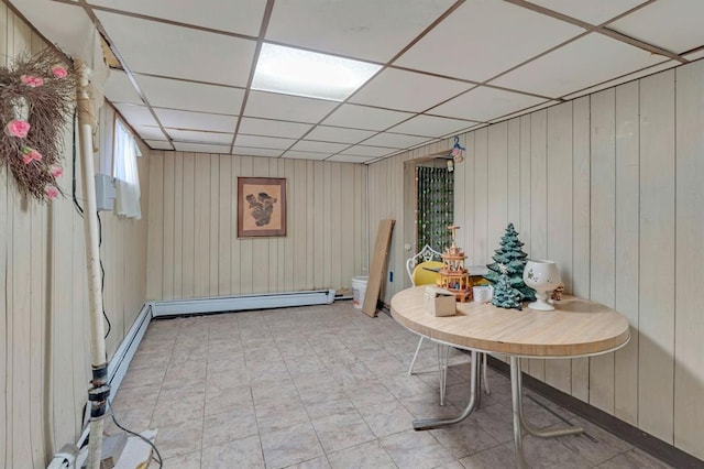 basement featuring a paneled ceiling, wood walls, and a baseboard heating unit