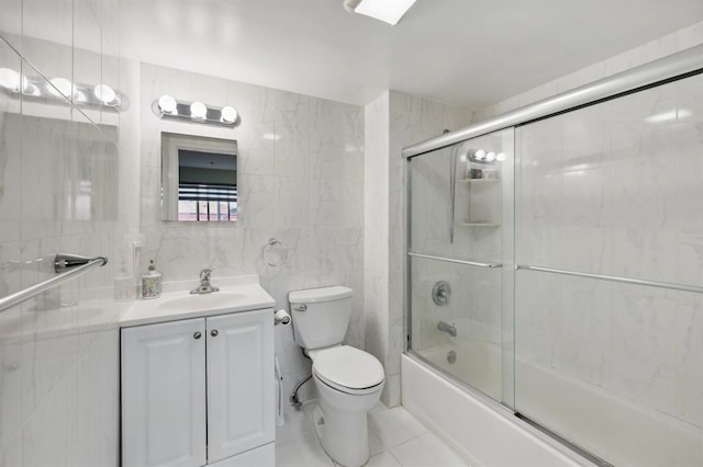 full bathroom with combined bath / shower with glass door, tile patterned floors, vanity, tile walls, and toilet