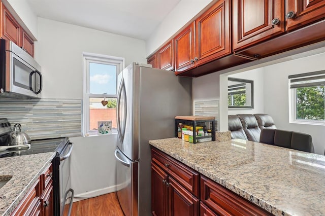 kitchen with tasteful backsplash, a wealth of natural light, light stone countertops, and appliances with stainless steel finishes