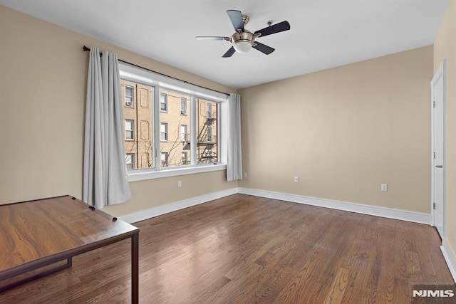 empty room featuring dark wood-style floors, baseboards, and a ceiling fan