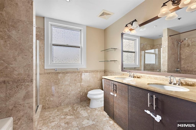 bathroom with tiled shower, a sink, visible vents, and tile walls