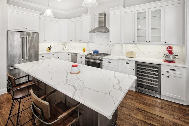 kitchen with a breakfast bar, high end appliances, beverage cooler, wall chimney range hood, and hanging light fixtures