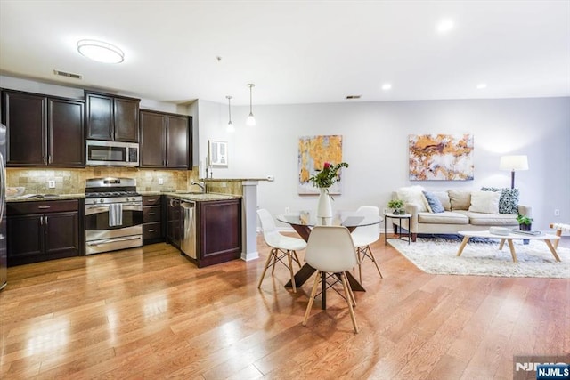 kitchen featuring pendant lighting, decorative backsplash, light stone counters, stainless steel appliances, and light hardwood / wood-style flooring