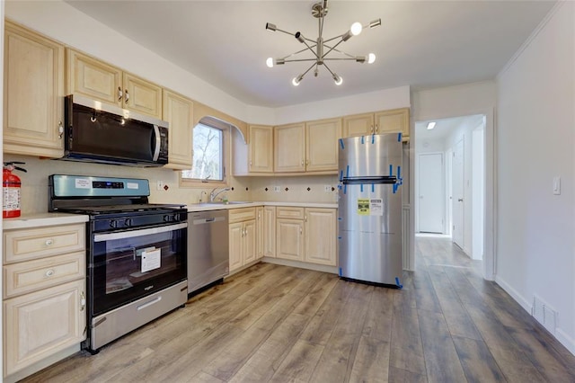 kitchen featuring light brown cabinetry, stainless steel appliances, sink, light hardwood / wood-style flooring, and a chandelier