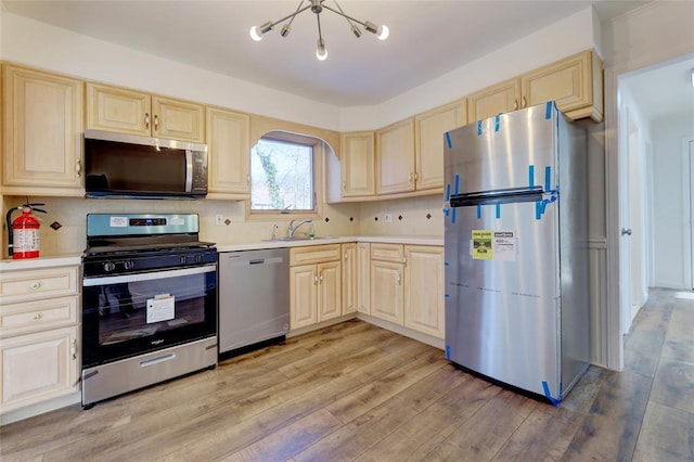 kitchen with sink, a chandelier, decorative backsplash, appliances with stainless steel finishes, and light wood-type flooring