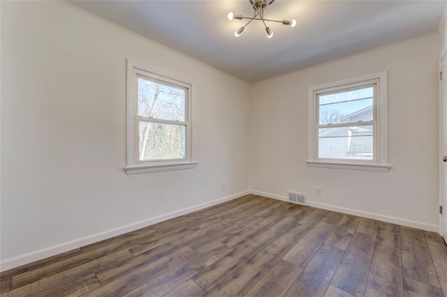 empty room with dark hardwood / wood-style flooring, an inviting chandelier, and a wealth of natural light