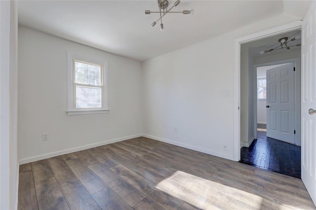 empty room with dark wood-type flooring and a notable chandelier