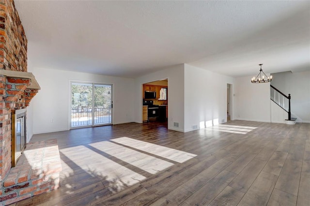 unfurnished living room with dark wood-type flooring, a notable chandelier, and a brick fireplace