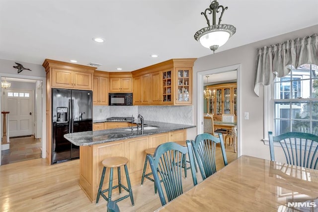 kitchen with a kitchen breakfast bar, dark stone countertops, decorative light fixtures, decorative backsplash, and black appliances