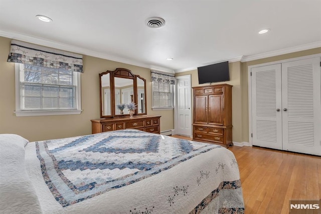 bedroom with a closet, light hardwood / wood-style floors, baseboard heating, and crown molding