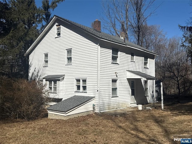 rear view of house featuring a chimney and roof with shingles