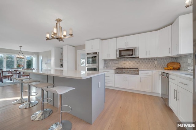 kitchen with decorative light fixtures, white cabinetry, a center island, tasteful backsplash, and appliances with stainless steel finishes