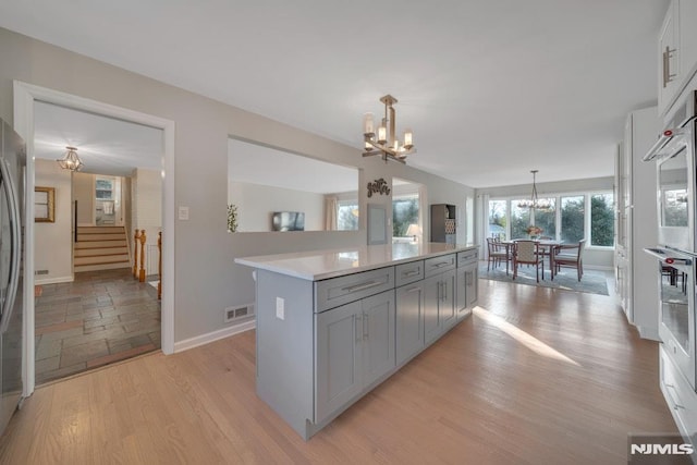 kitchen featuring gray cabinets, hanging light fixtures, light wood-type flooring, a center island, and a notable chandelier