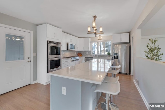 kitchen with a chandelier, stainless steel appliances, pendant lighting, a kitchen island, and white cabinets