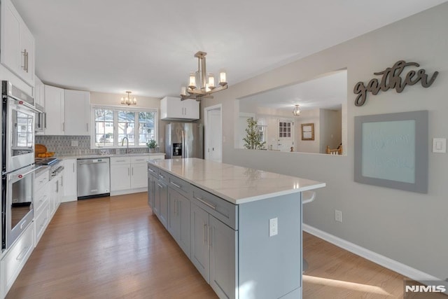 kitchen with sink, decorative light fixtures, white cabinetry, a kitchen island, and appliances with stainless steel finishes