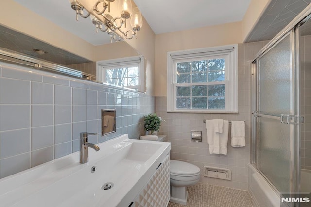 full bathroom featuring toilet, combined bath / shower with glass door, tile walls, tile patterned floors, and sink