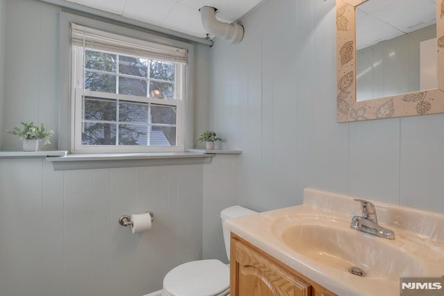 bathroom with toilet, vanity, and wood walls