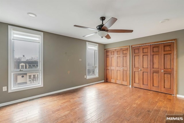 unfurnished bedroom featuring ceiling fan, light hardwood / wood-style floors, and multiple closets