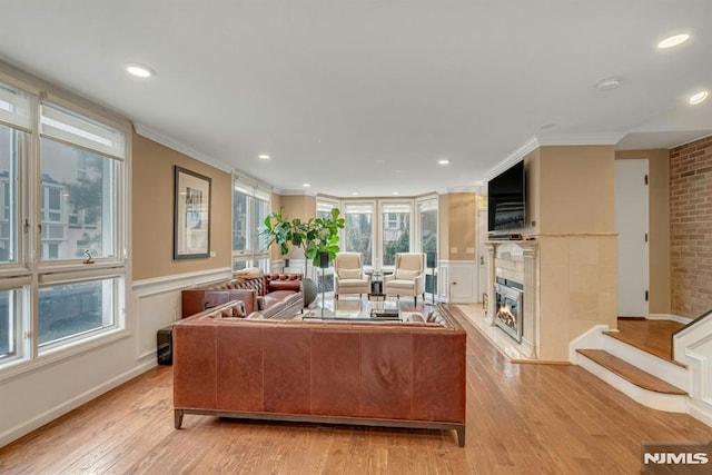 living room with a wealth of natural light, a fireplace, ornamental molding, and light hardwood / wood-style floors