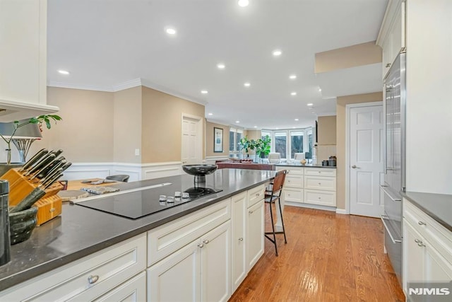 kitchen featuring a kitchen breakfast bar, black electric stovetop, ornamental molding, light hardwood / wood-style flooring, and white cabinetry