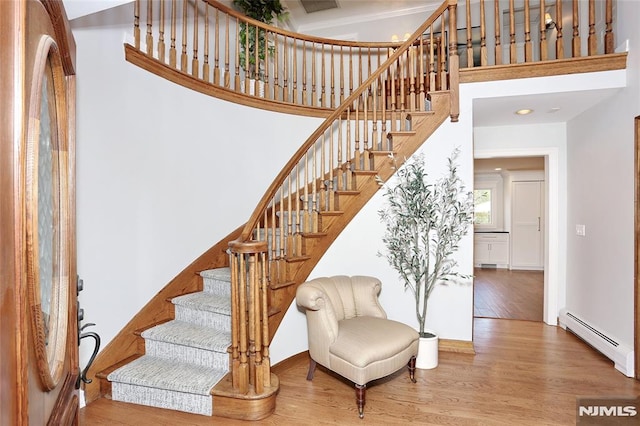 stairs featuring hardwood / wood-style flooring, baseboard heating, and a towering ceiling