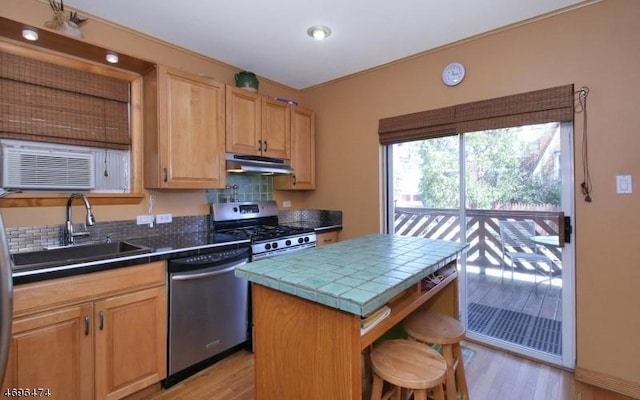 kitchen with sink, a center island, tile countertops, appliances with stainless steel finishes, and light wood-type flooring