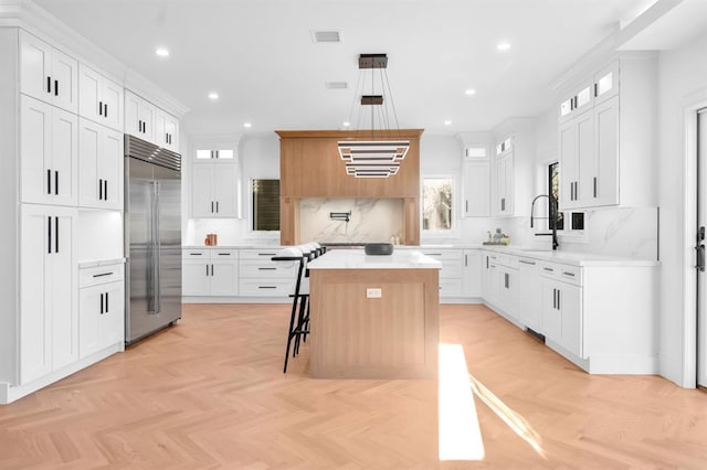 kitchen with a center island, white cabinets, stainless steel built in refrigerator, a breakfast bar, and light parquet flooring