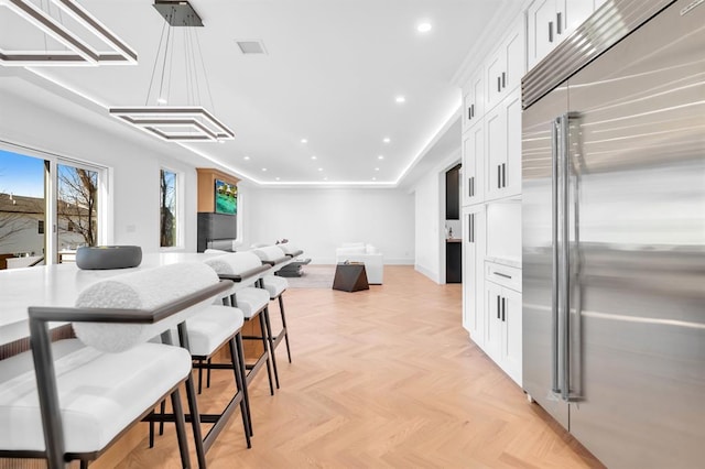 kitchen featuring white cabinetry, built in fridge, light parquet floors, and hanging light fixtures