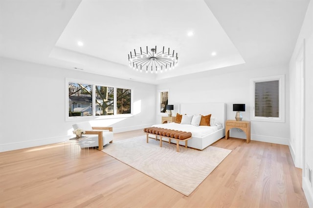 bedroom with a tray ceiling, light hardwood / wood-style floors, and an inviting chandelier