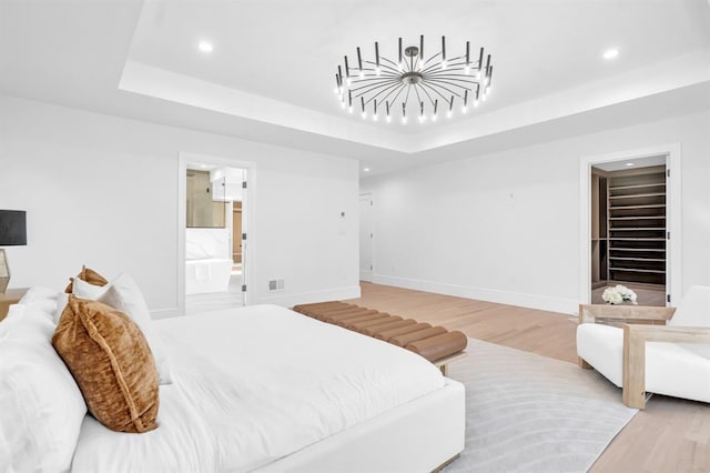 bedroom with ensuite bath, a tray ceiling, a walk in closet, a closet, and hardwood / wood-style flooring