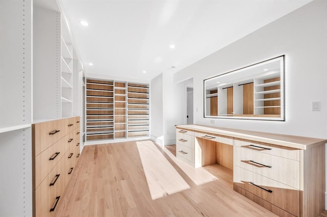 walk in closet featuring built in desk and light hardwood / wood-style floors