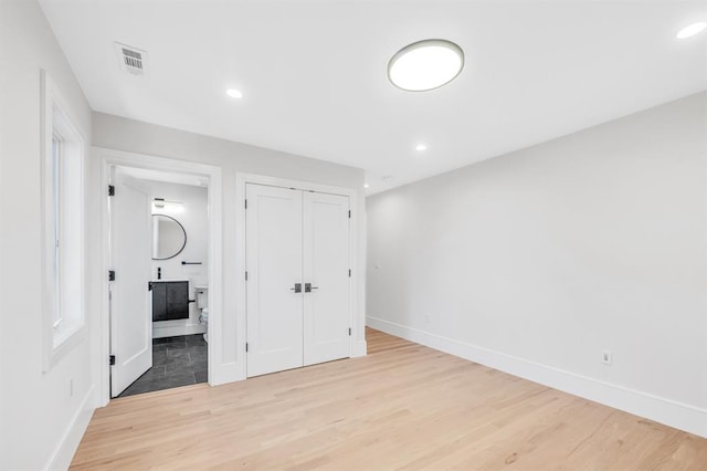 unfurnished bedroom with light wood-type flooring, ensuite bathroom, and a closet