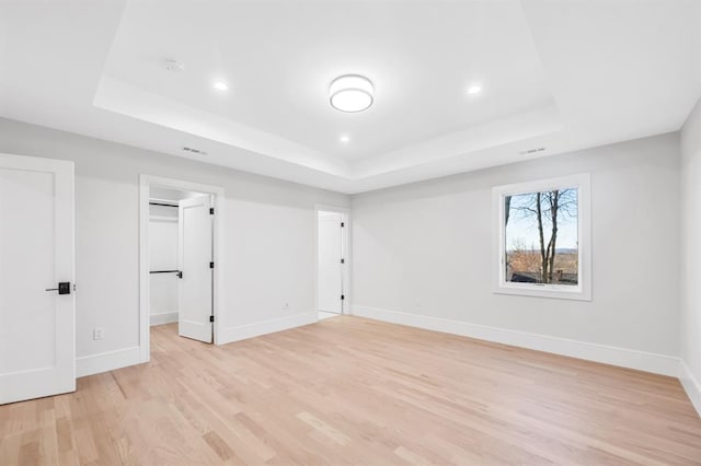 unfurnished bedroom featuring a raised ceiling, a walk in closet, and light wood-type flooring