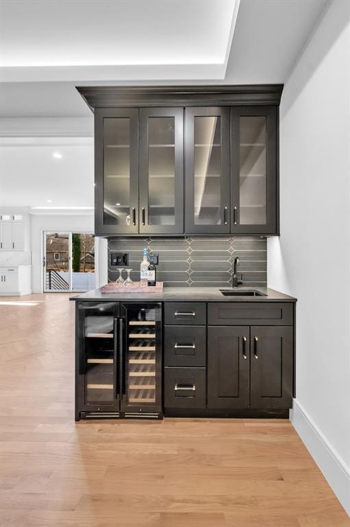 bar featuring tasteful backsplash, wine cooler, sink, and light hardwood / wood-style floors