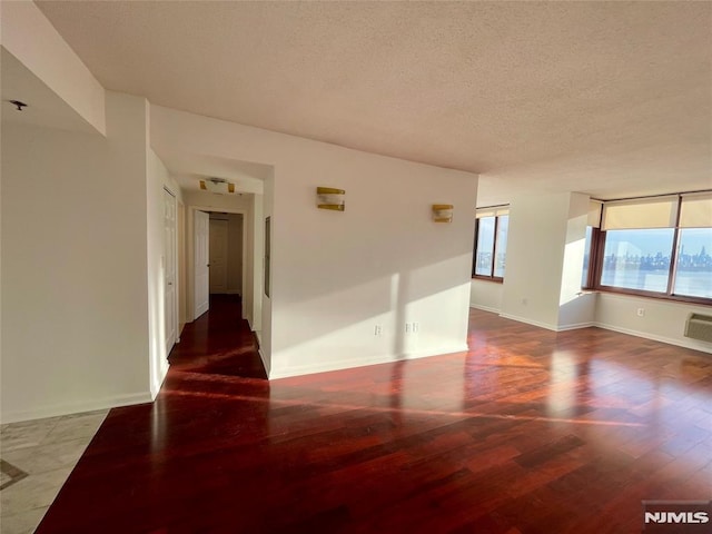 unfurnished room featuring a textured ceiling, a wall unit AC, and dark hardwood / wood-style floors