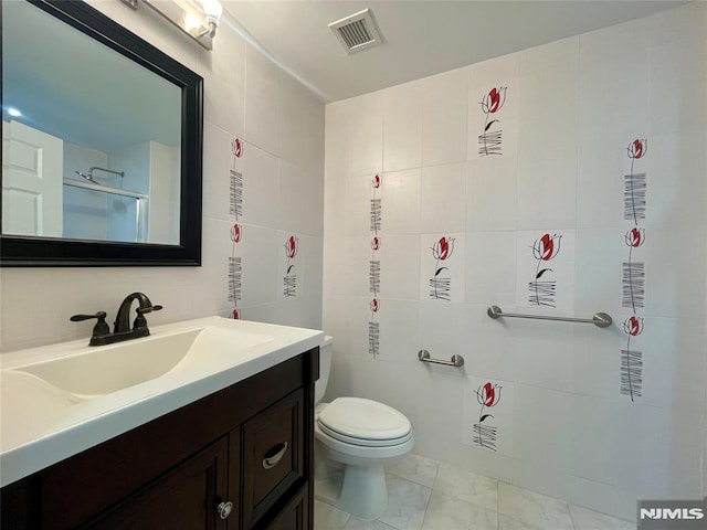 bathroom featuring walk in shower, vanity, toilet, and tile walls