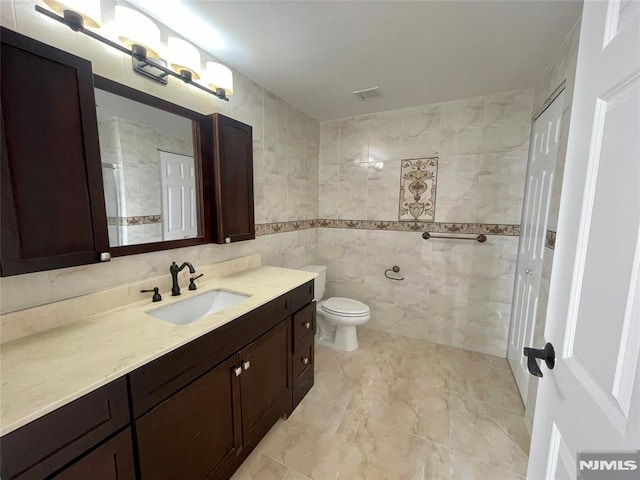 bathroom featuring vanity, toilet, and tile walls