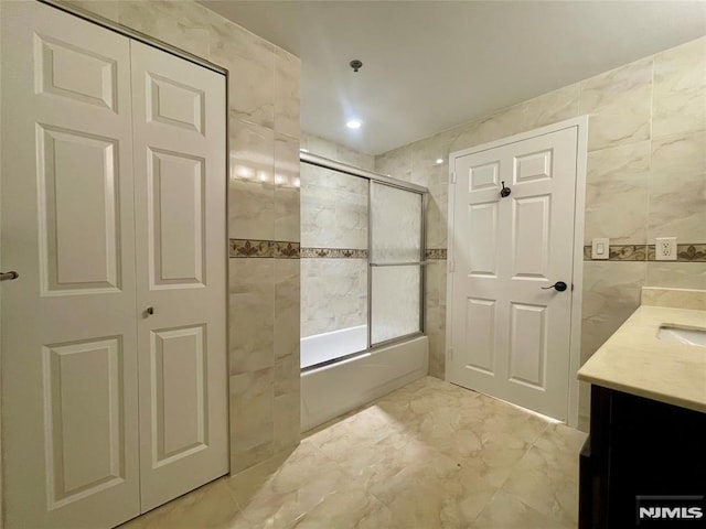 bathroom featuring vanity, bath / shower combo with glass door, and tile walls